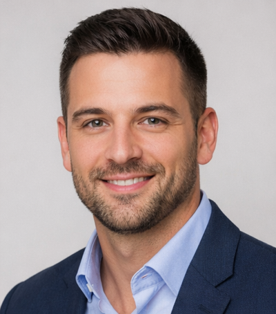 Man wearing a dark suit and light blue shirt against a plain background